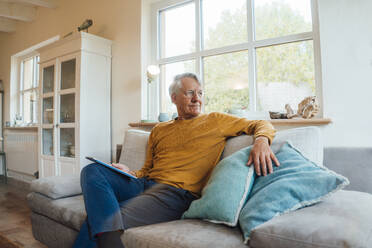 Älterer Mann mit Tablet-PC auf dem Sofa im heimischen Wohnzimmer sitzend - JOSEF16311