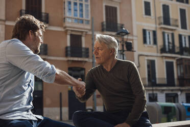 Älterer Mann schüttelt Hände mit Vater vor einem Gebäude sitzend - JOSEF16324