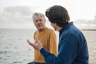 Man having discussion with father in front of sea - JOSEF16377