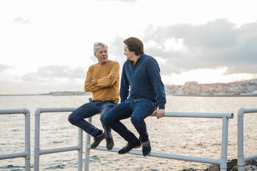 Vater und Sohn diskutieren zusammen auf dem Geländer sitzend - JOSEF16380