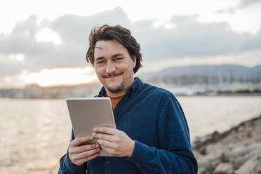 Mann mit Tablet-PC vor dem Meer stehend - JOSEF16382