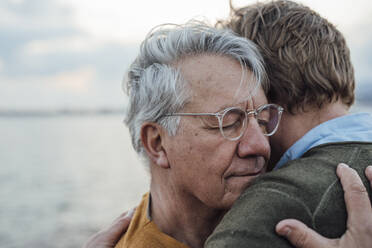 Lächelnder älterer Mann mit grauem Haar, der seinen Sohn umarmt - JOSEF16395