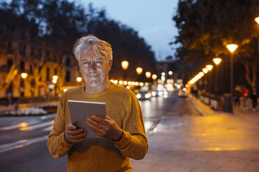 Smiling senior man standing with tablet PC at footpath - JOSEF16405