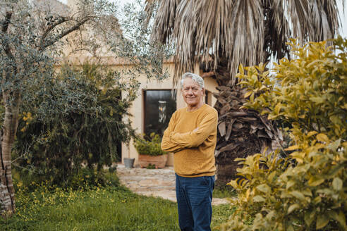 Smiling senior man standing with arms crossed in back yard - JOSEF16406