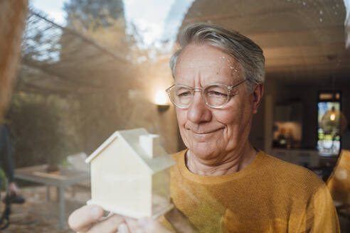 Lächelnder älterer Mann mit Modellhaus durch Glas gesehen - JOSEF16424