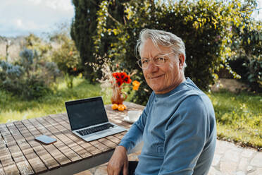 Lächelnder älterer Mann mit Laptop am Tisch sitzend - JOSEF16455