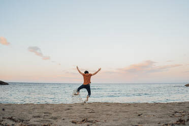 Carefree man jumping in front of sea at sunset - JOSEF16494