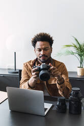 Businessman with camera sitting at desk in office - PNAF04905