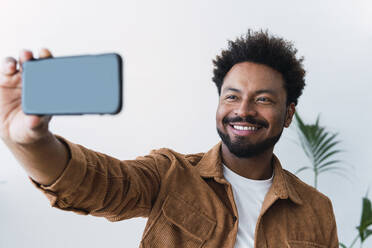 Glücklicher Geschäftsmann, der ein Selfie mit seinem Mobiltelefon vor einer Wand macht - PNAF04917