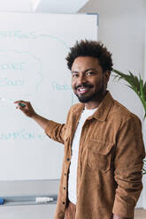 Lächelnder Geschäftsmann, der vor einem Whiteboard im Büro steht und eine Strategie plant - PNAF04927