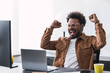 Successful businessman cheering at desk in office - PNAF04933