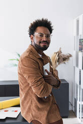 Smiling businessman wearing eyeglasses standing with laptop in office - PNAF04936