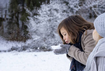Cute girl blowing snow on hand by sister - LBF03708