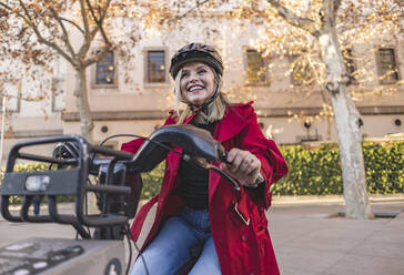 Glückliche reife Frau mit Helm fährt Fahrrad auf der Straße - JCCMF09047