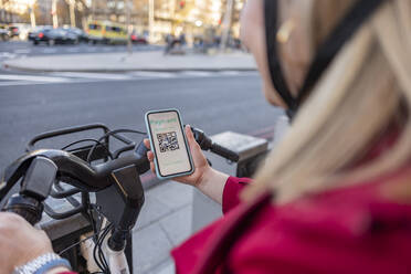Frau scannt QR-Code eines Fahrrads mit Smartphone auf der Straße - JCCMF09049