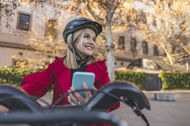 Glückliche reife Frau mit Smartphone auf dem Fahrrad - JCCMF09050