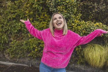 Carefree mature woman wearing pink sweater dancing in front of plants - JCCMF09065