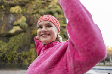 Happy mature woman in pink sweater flexing muscles - JCCMF09069