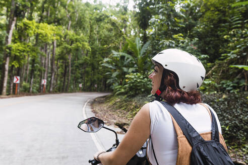 Happy young woman wearing helmet riding motorcycle - PNAF04956