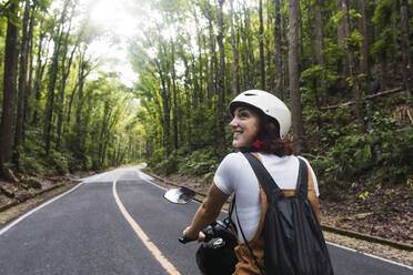 Glückliche Frau mit Helm beim Motorradfahren auf der Straße - PNAF04963