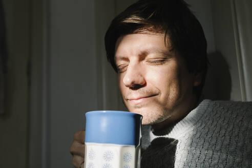Smiling man with eyes closed holding cup of tea at home - TYF00689