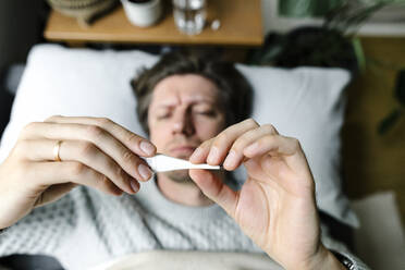 Man looking at thermometer lying on bed at home - TYF00694