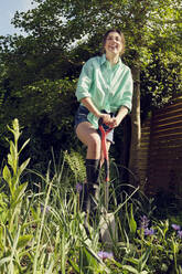 Glückliche Frau mit Schaufel bei der Gartenarbeit im Garten - PWF00674