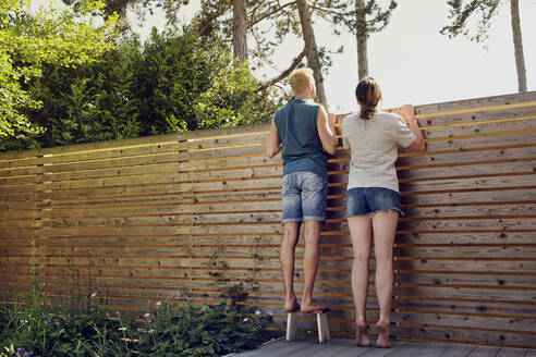 Young couple looking over wooden fence at back yard - PWF00681