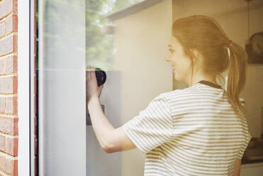 Young woman adjusting thermostat seen through glass - PWF00689