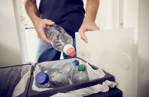 Young man recycling plastic bottles at home - PWF00693