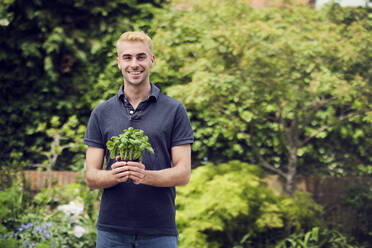Lächelnder junger Mann hält Pflanze im Hinterhof - PWF00733