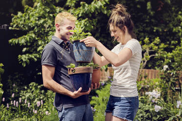 Glückliche Frau hilft ihrem Freund beim Tragen von Topfpflanzen im Hinterhof - PWF00735