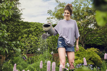 Lächelnde Frau beim Gießen von Pflanzen im Hinterhof stehend - PWF00742