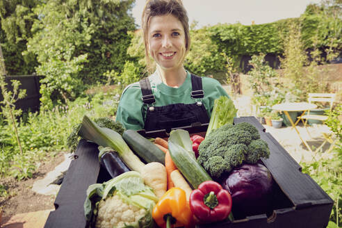 Smiling young delivery person with box of fresh vegetables - PWF00745