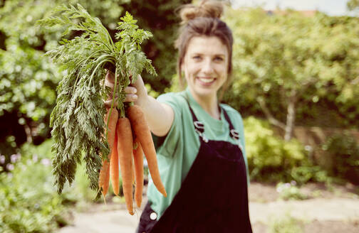 Happy young woman holding bunch of fresh organic carrots - PWF00749