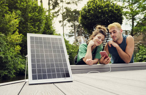 Couple sharing smart phone being charged by solar panel - PWF00751