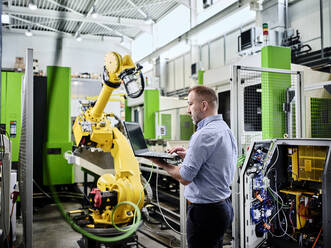 Techniker mit Laptop am Roboterarm in einer modernen Fabrik - CVF02284