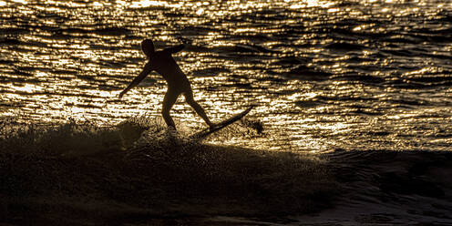 Silhouette Mann beim Surfen auf dem Meer bei Sonnenuntergang, Pembrokeshire, Wales - ALRF01937