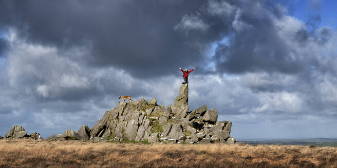 Mann mit erhobenen Armen auf einem Felsen stehend unter bewölktem Himmel, Preseli Hills, Pembrokeshire, Wales - ALRF01972