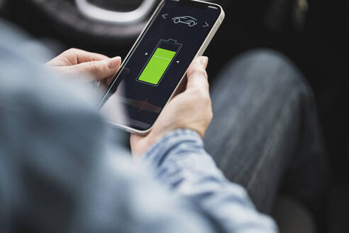 Hands of woman using mobile app to operate electric car - UUF28033