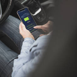 Hand of woman operating electric car through mobile app on smart phone - UUF28038