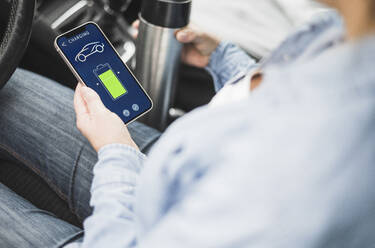 Hand of woman using electric car charging app on smart phone - UUF28041