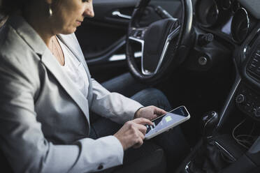 Ältere Frau, die eine App zum Aufladen von Elektroautos auf ihrem Mobiltelefon untersucht - UUF28058