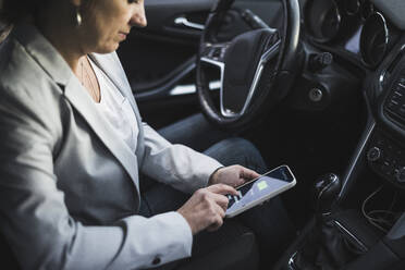 Mature woman examining electric car charging app on mobile phone - UUF28058