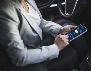 Hands of woman examining electric car charging app on mobile phone - UUF28059