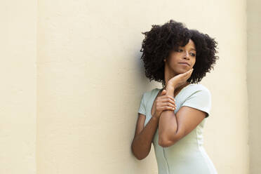 Nachdenkliche junge Frau mit Afrofrisur an der Wand stehend - LMCF00011