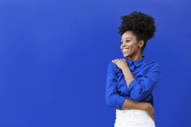 Glückliche junge Frau mit Afrofrisur auf blauem Hintergrund - LMCF00016