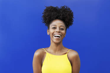 Young woman with Afro hairstyle laughing over blue background - LMCF00019