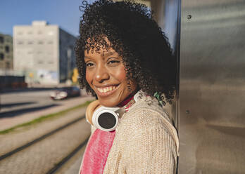 Happy young woman with wireless headphones at station - JCCMF09076