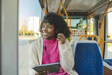 Happy young woman wearing In-ear headphones holding tablet PC in tram - JCCMF09083